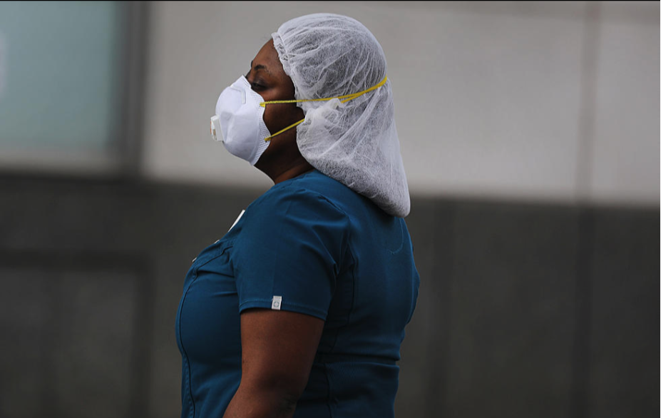 A woman wears a face mask, Scrubs, and hair covering PPE